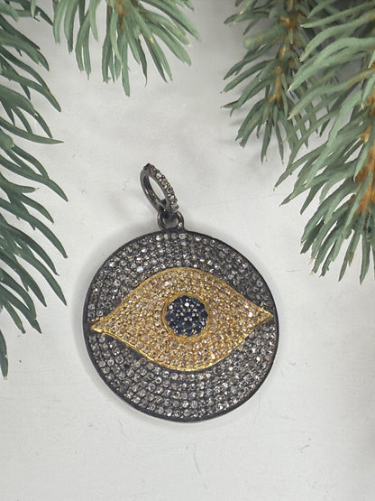 Pave diamond pendant with eye design on a white surface with greenery