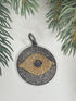 Pave diamond pendant with eye design on a white surface with greenery