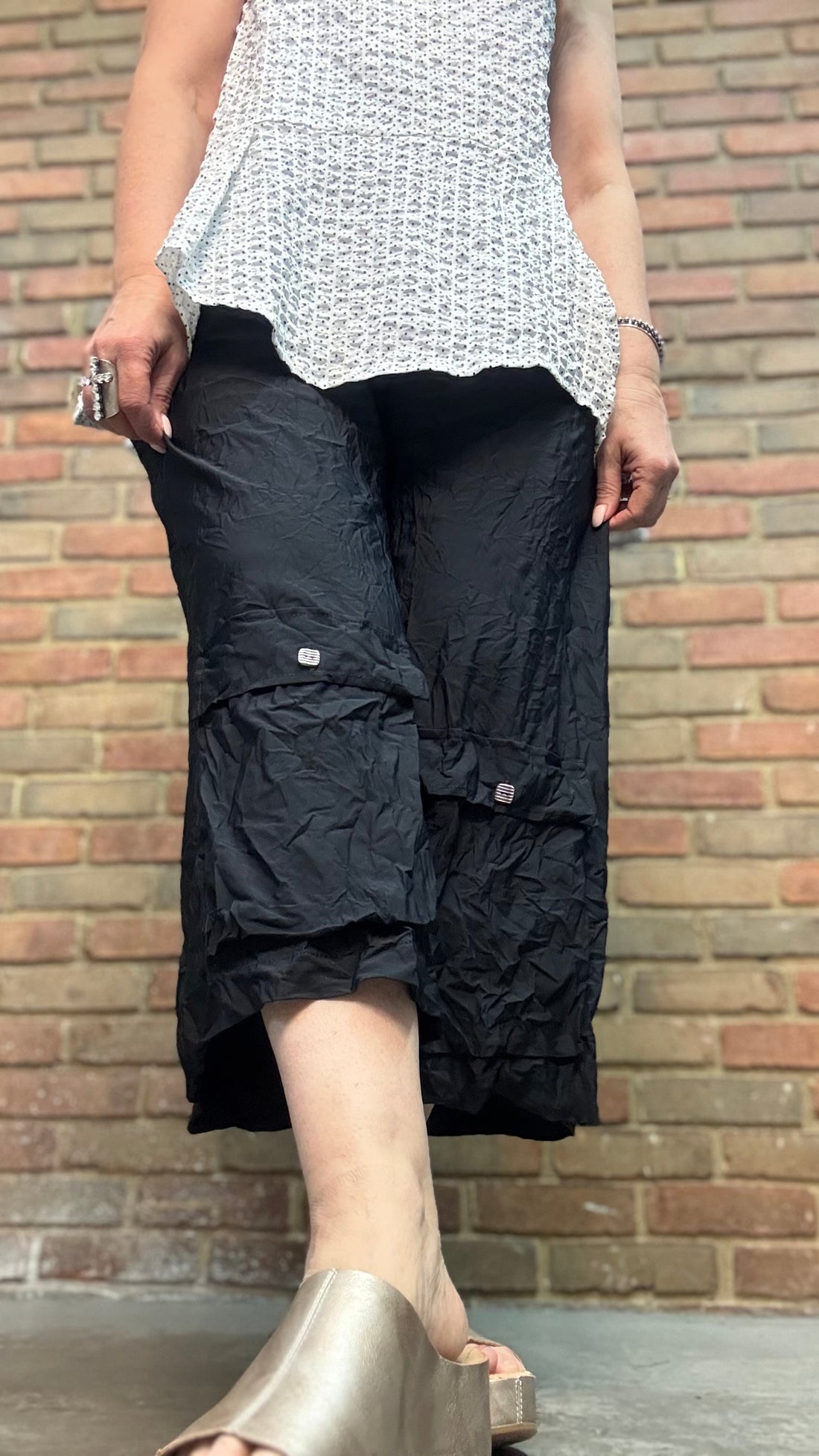 Person wearing a white patterned top and Lissie Pant - Blacks against a brick wall.