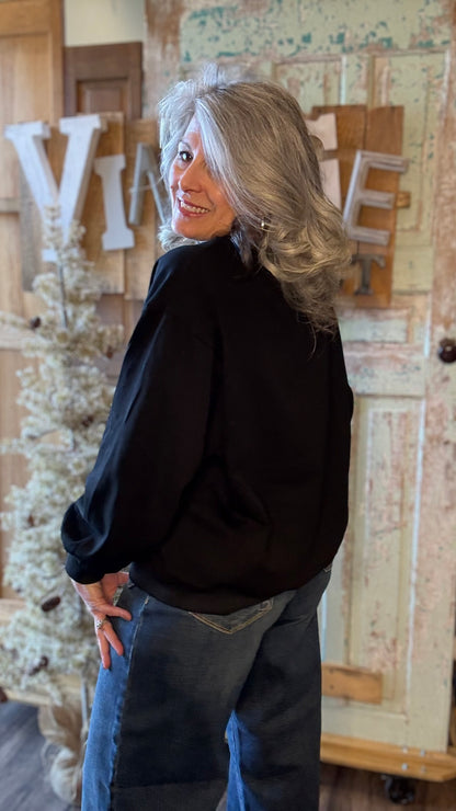 Woman in a black sweater and jeans standing in a rustic indoor setting with decorative elements.