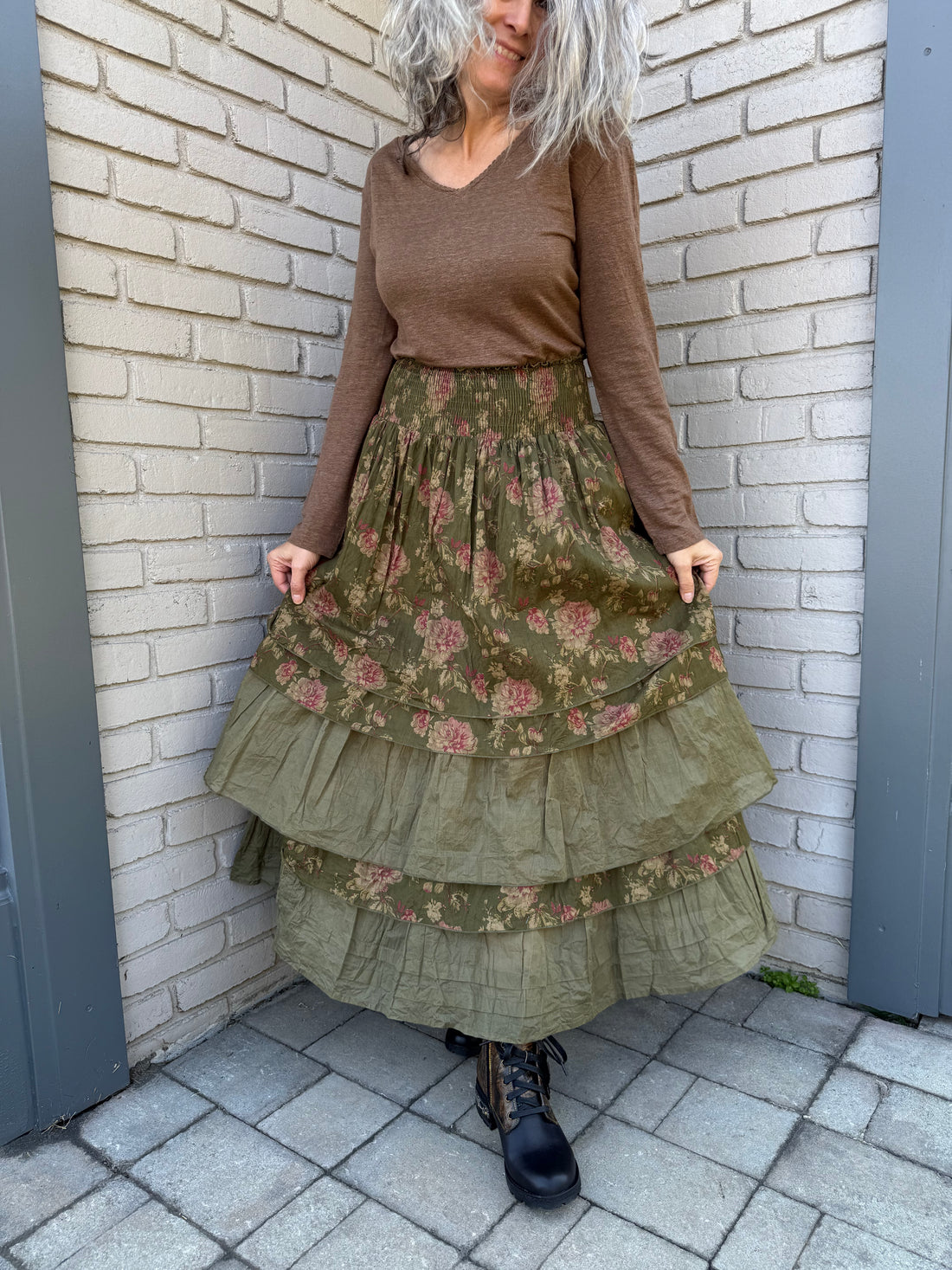 Person wearing a long green floral dress on a brick pavement.