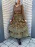 Person wearing a long green floral dress on a brick pavement.