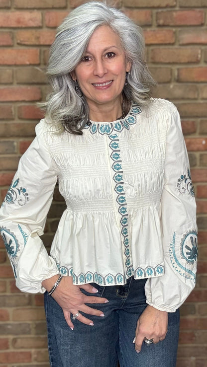 Woman wearing the Embroideried Smocked Peasant Top and Judy Blue Palazzo jeans against a brick wall.