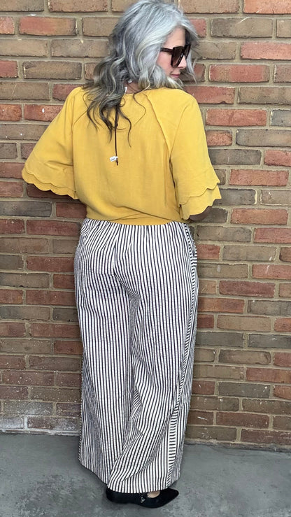 Woman in a mustard and Latte Wide Leg Pull On Pant standing against a brick wall.