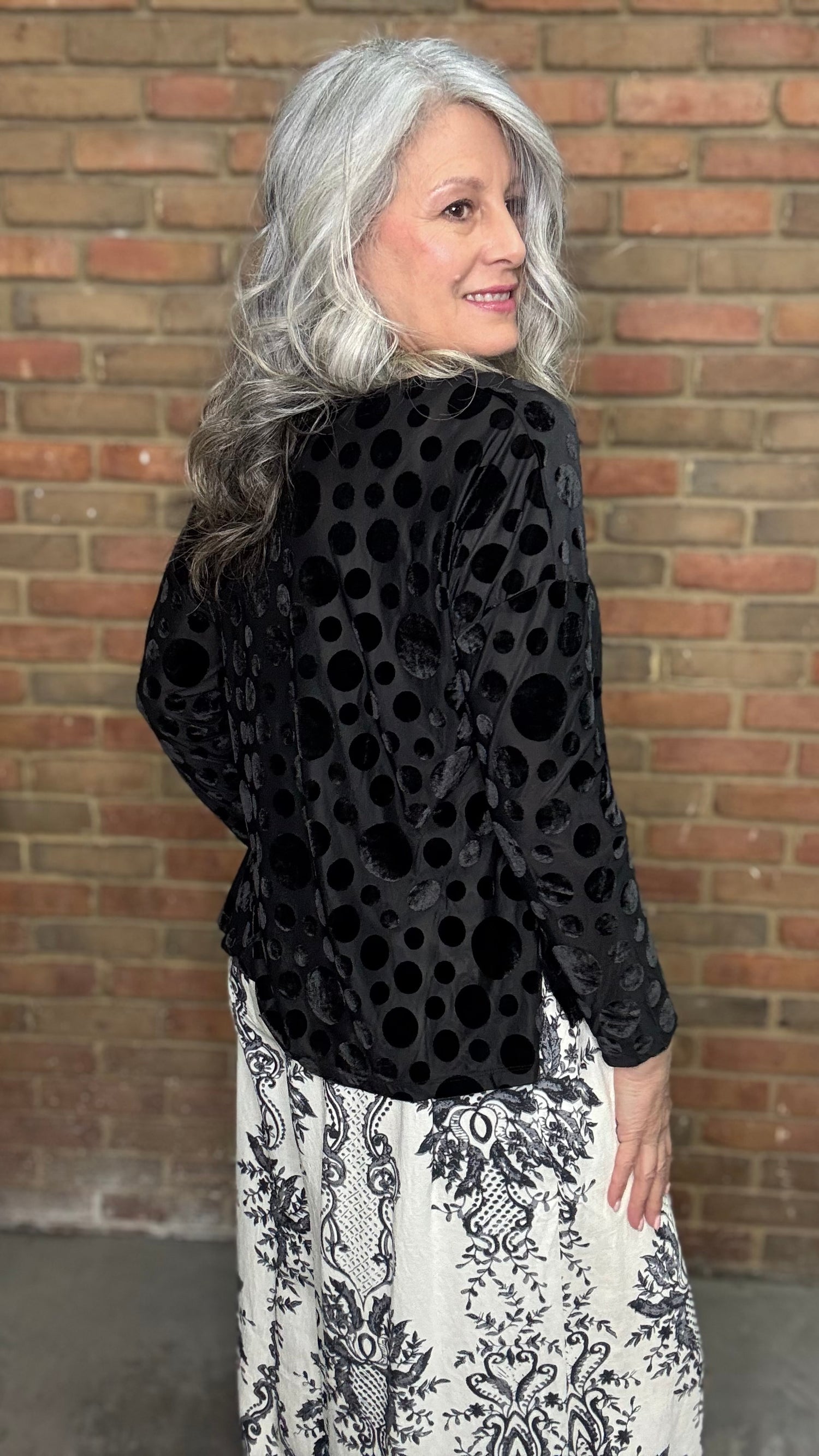 Woman wearing Black Velvet Burnout Top, Floral Print Wide Leg Pant against a brick wall. 