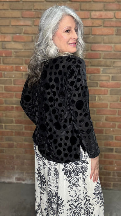 Woman wearing Black Velvet Burnout Top, Floral Print Wide Leg Pant against a brick wall. 