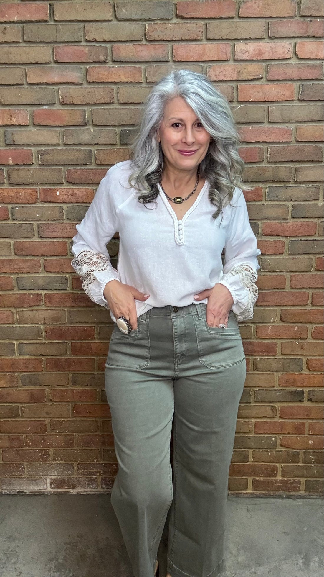 Woman wearing Cropped Wide Leg Twill Pants  Sage and a white blouse against a brick wall.