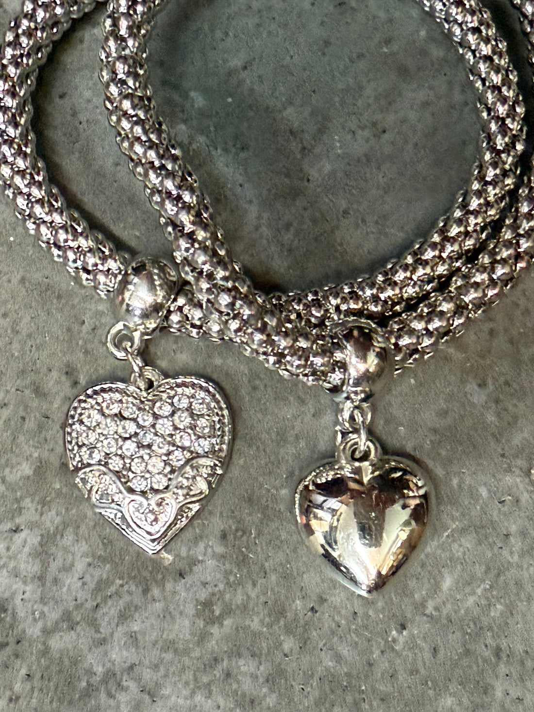 Silver bracelet with heart-shaped pendants on a concrete surface