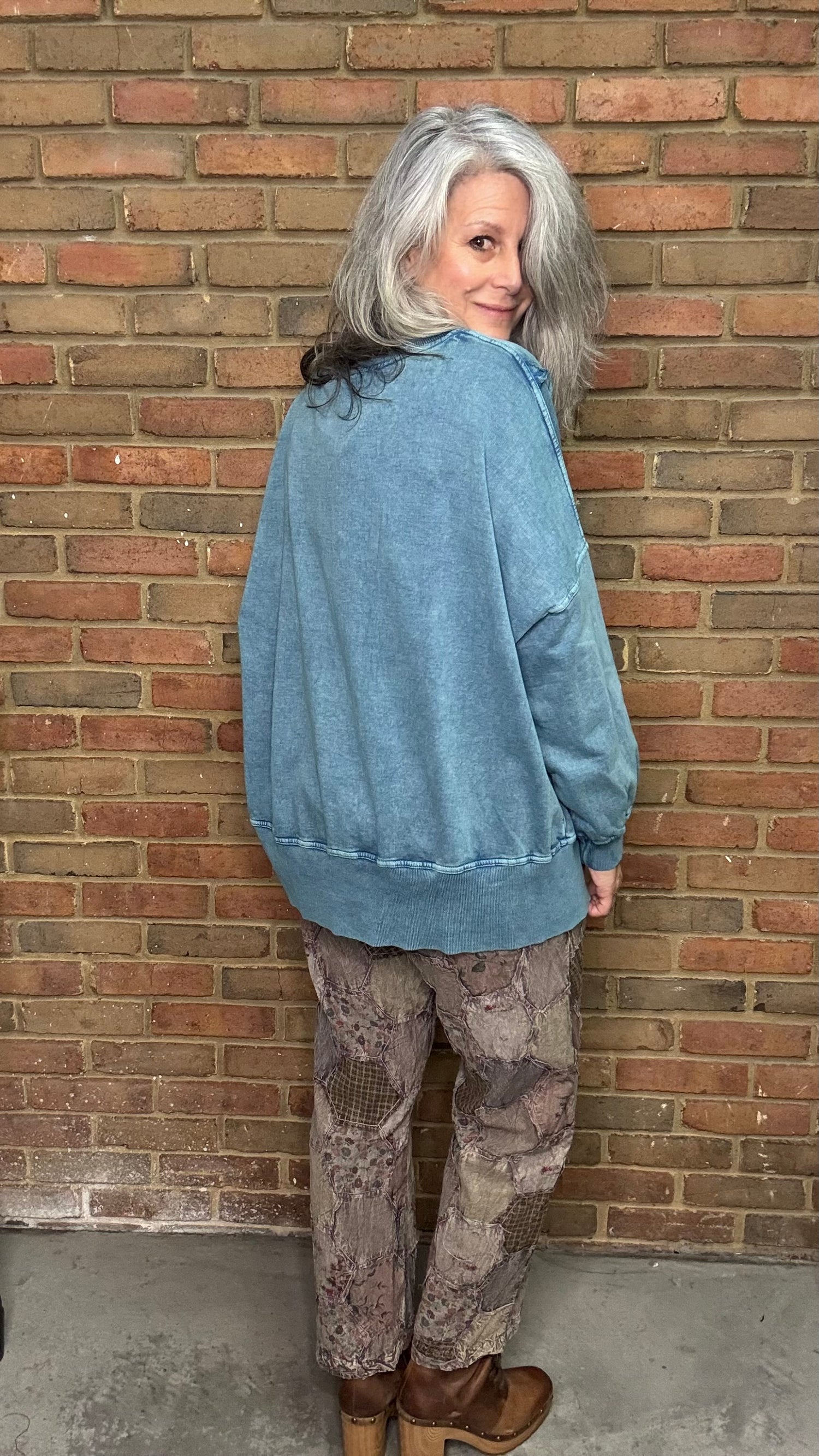 Person wearing a blue jacket and camouflage pants standing against a brick wall.