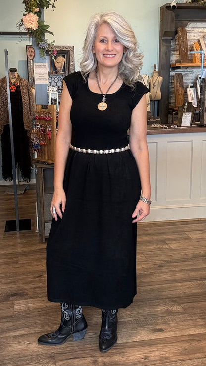 Woman in a black dress standing in a store with mannequins and clothing in the background.