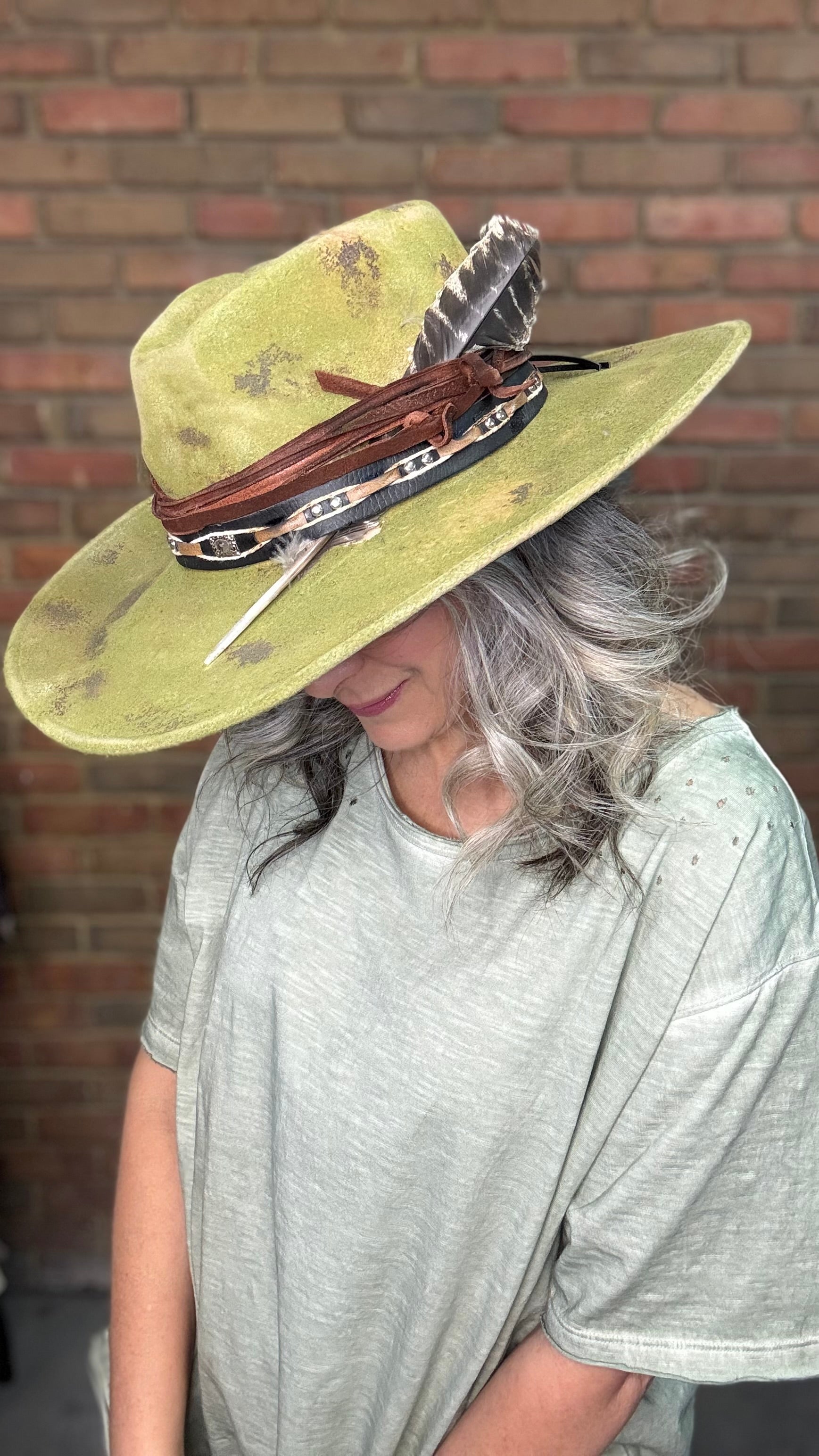 Woman wearing Spirit Feather Hat against a brick wall.