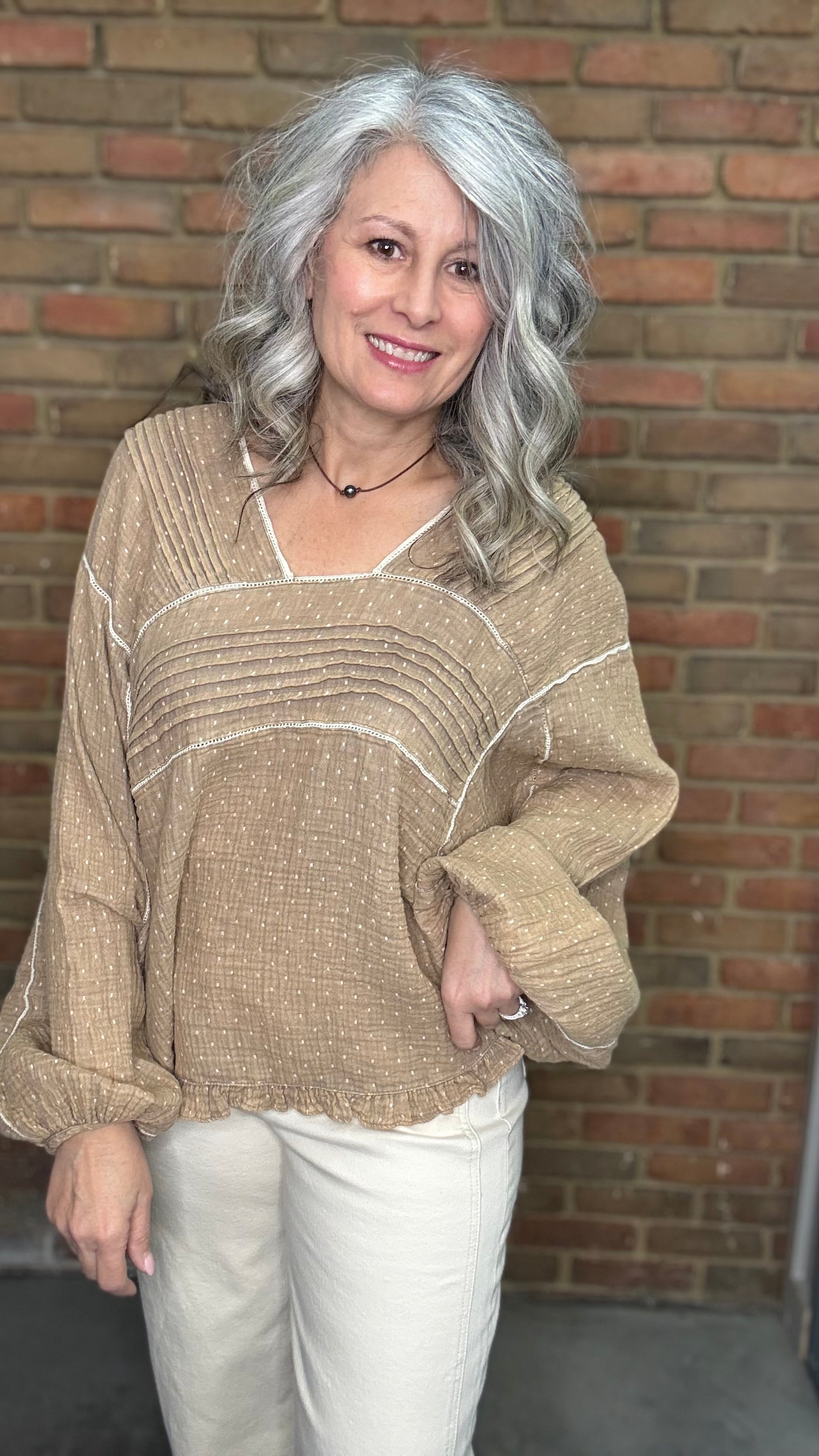 Woman wearing Mocha and Ivory Print Long Sleeve Top and blue jeans standing against a brick wall.