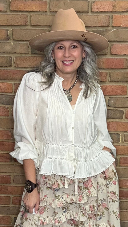 Woman in a White Pin-Tuck Lace Embellished shirt, blooming romance skirt, and Kate Harness Frye boots standing against a brick wall.