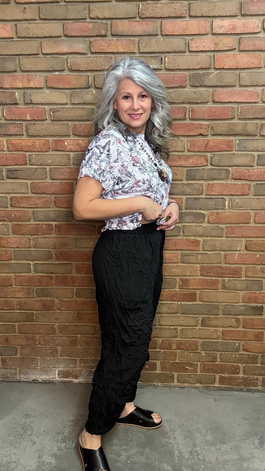 Person wearing Black Crinkle Side Pocket Pant and a patterned top against a brick wall.