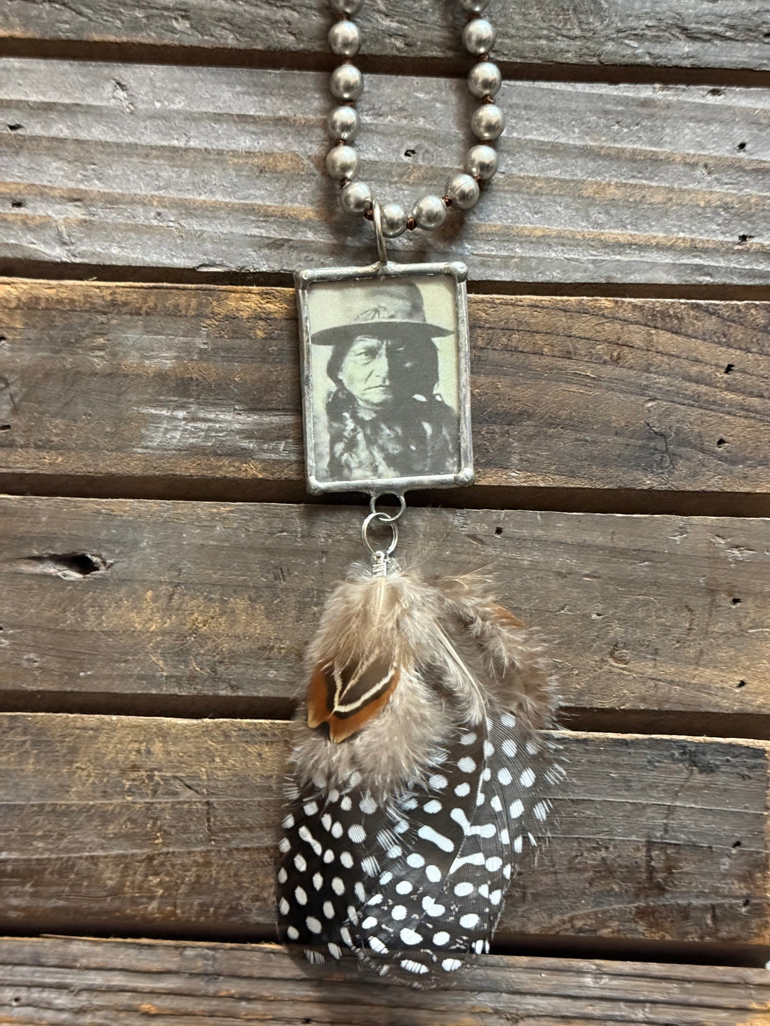Necklace with feather and vintage-style photo pendant on wooden surface