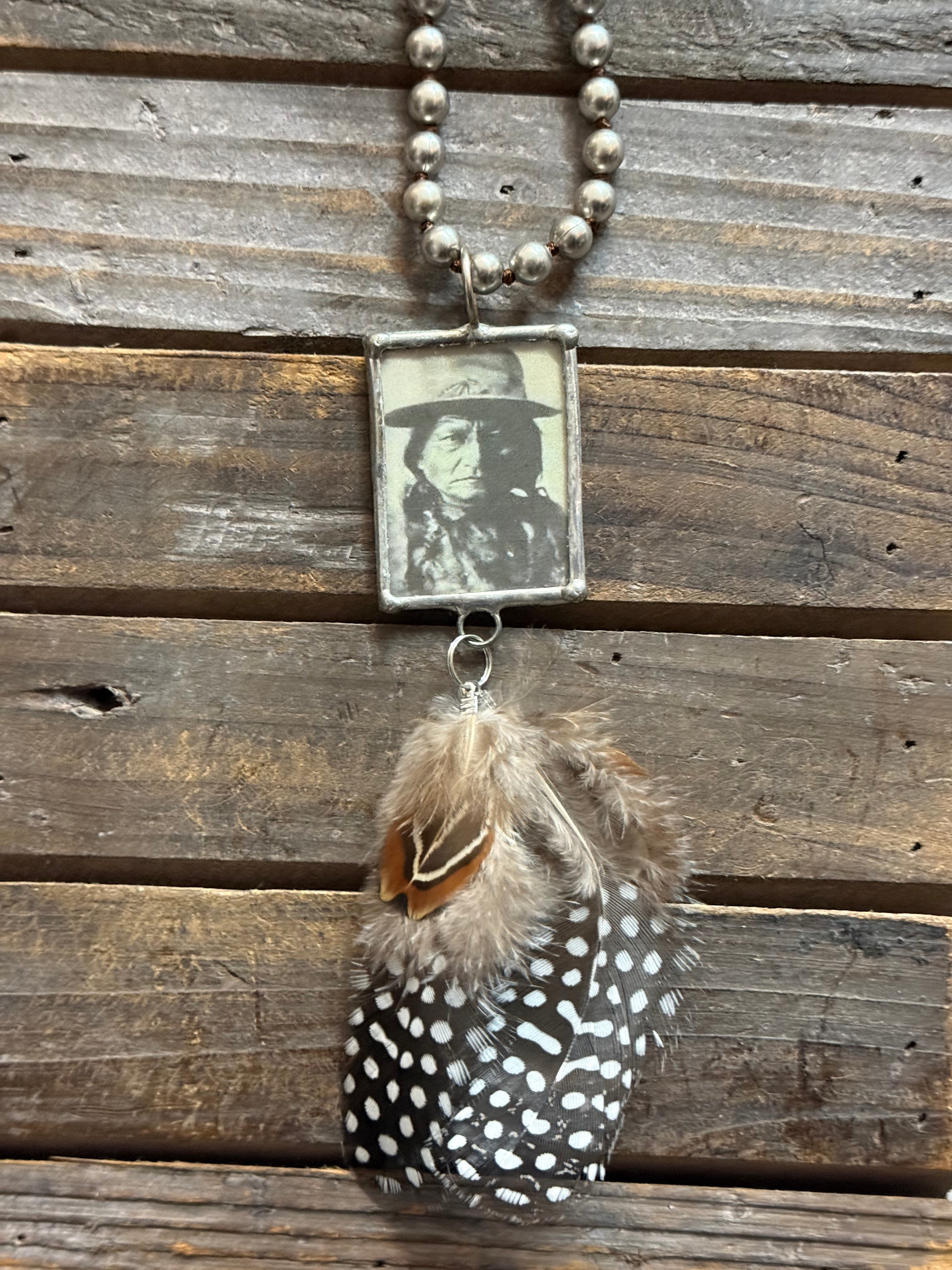 Necklace with feather and vintage-style photo pendant on wooden surface