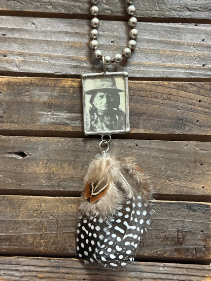 Necklace with feather and vintage-style photo pendant on wooden surface