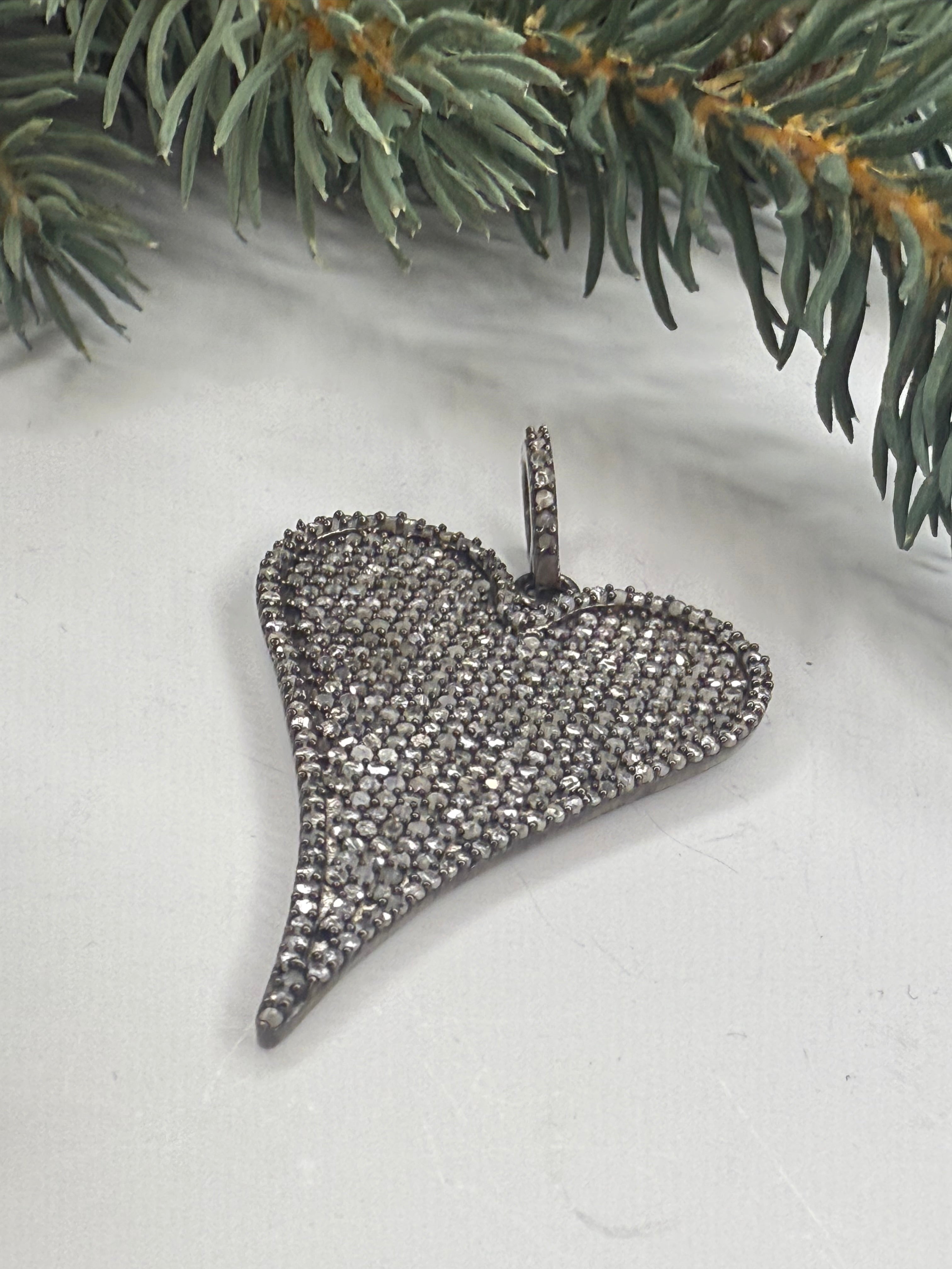 Silver heart shaped pendant with pave diamonds on a white surface with greenery