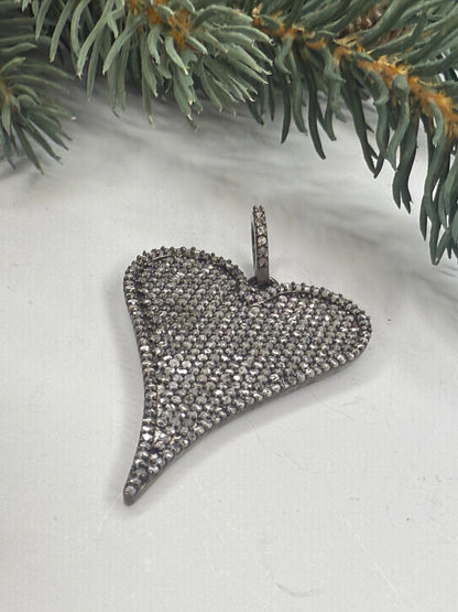Silver heart shaped pendant with pave diamonds on a white surface with greenery