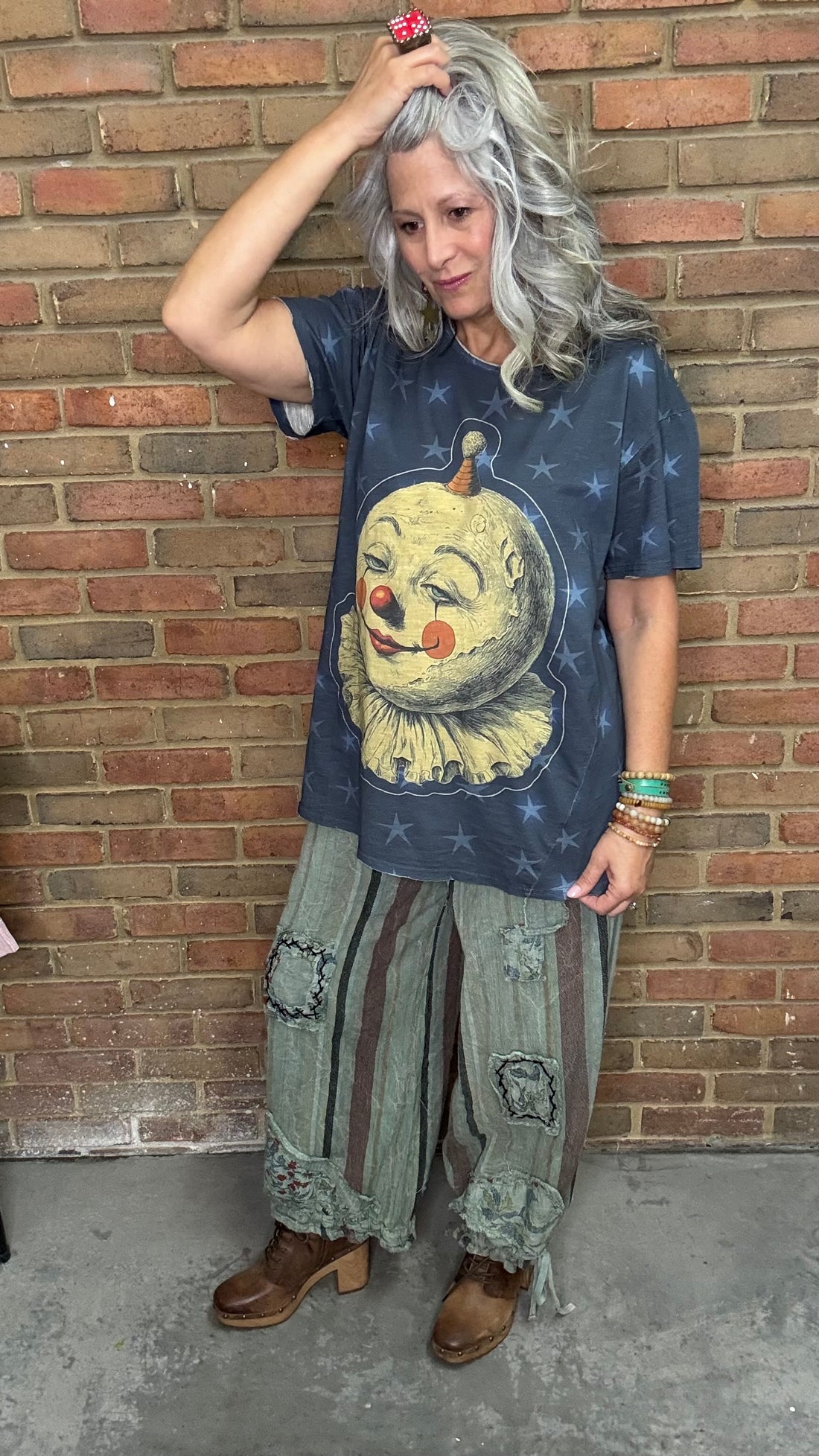 Woman wearing a Moon Dance Tee - Moon Wander with a clown graphic design in front of a brick wall.