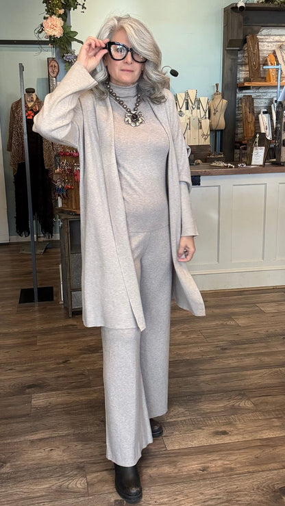 Woman in a beige outfit standing in a store with clothing racks and displays in the background.