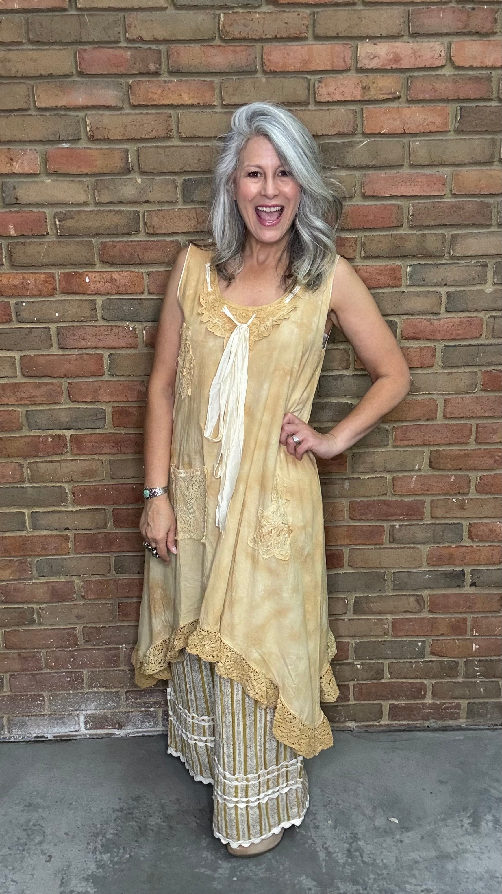 Woman wearing the Wandering Spirit Dress a tea stained tank dress with striped pants standing in front of a brick wall.