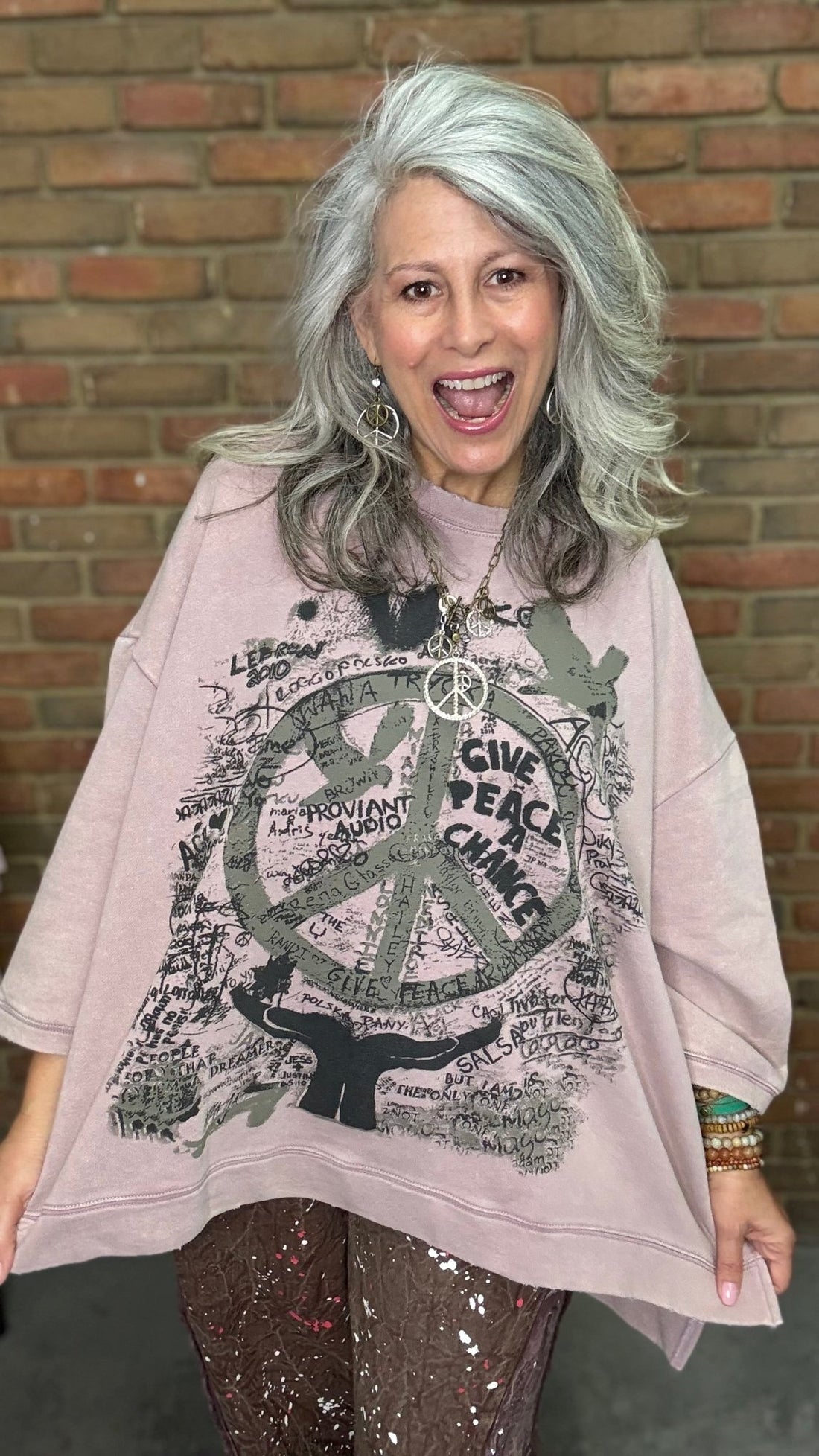 Woman wearing oversized plum sweatshirt with peace graffiti in front of brick wall.