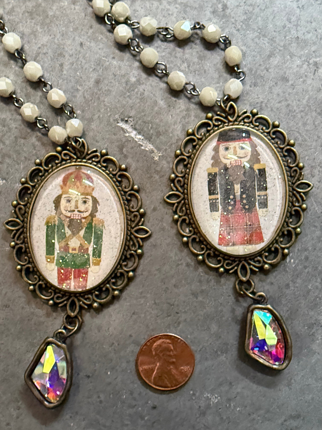 Two ornate necklaces with pendant images of a person in a suit on a gray surface.