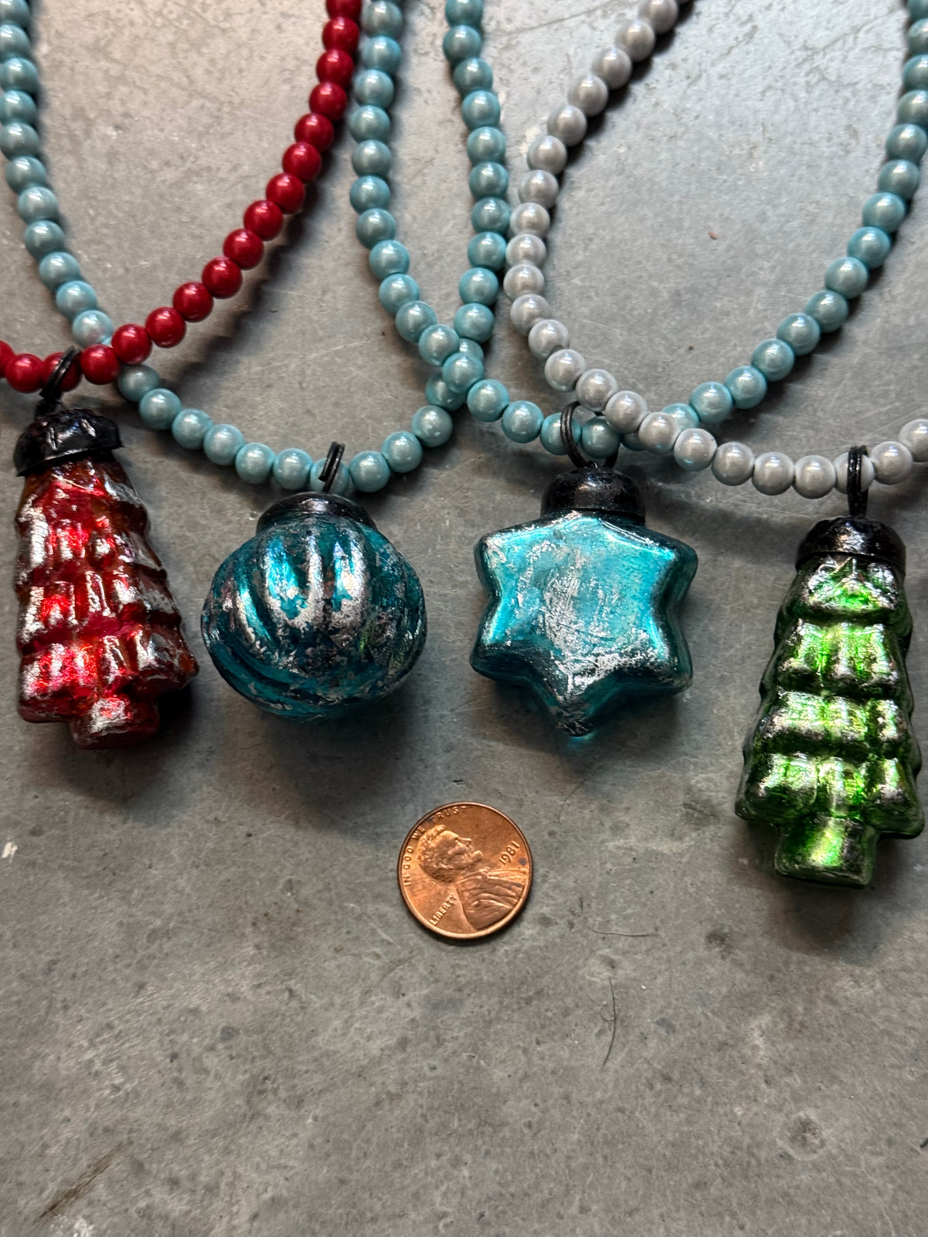 Close-up of beaded necklaces with decorative pendants on a gray surface, with a penny for scale.