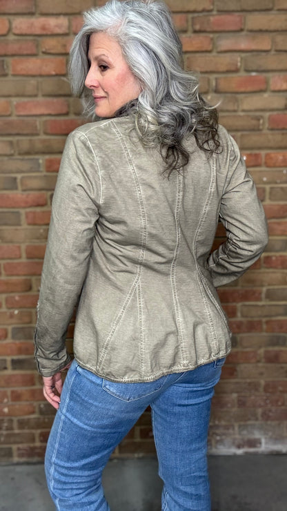 Woman wearing the Colonel Jacket in Taupe with a Sacred Heart Charm Necklace standing in front of brick wall.