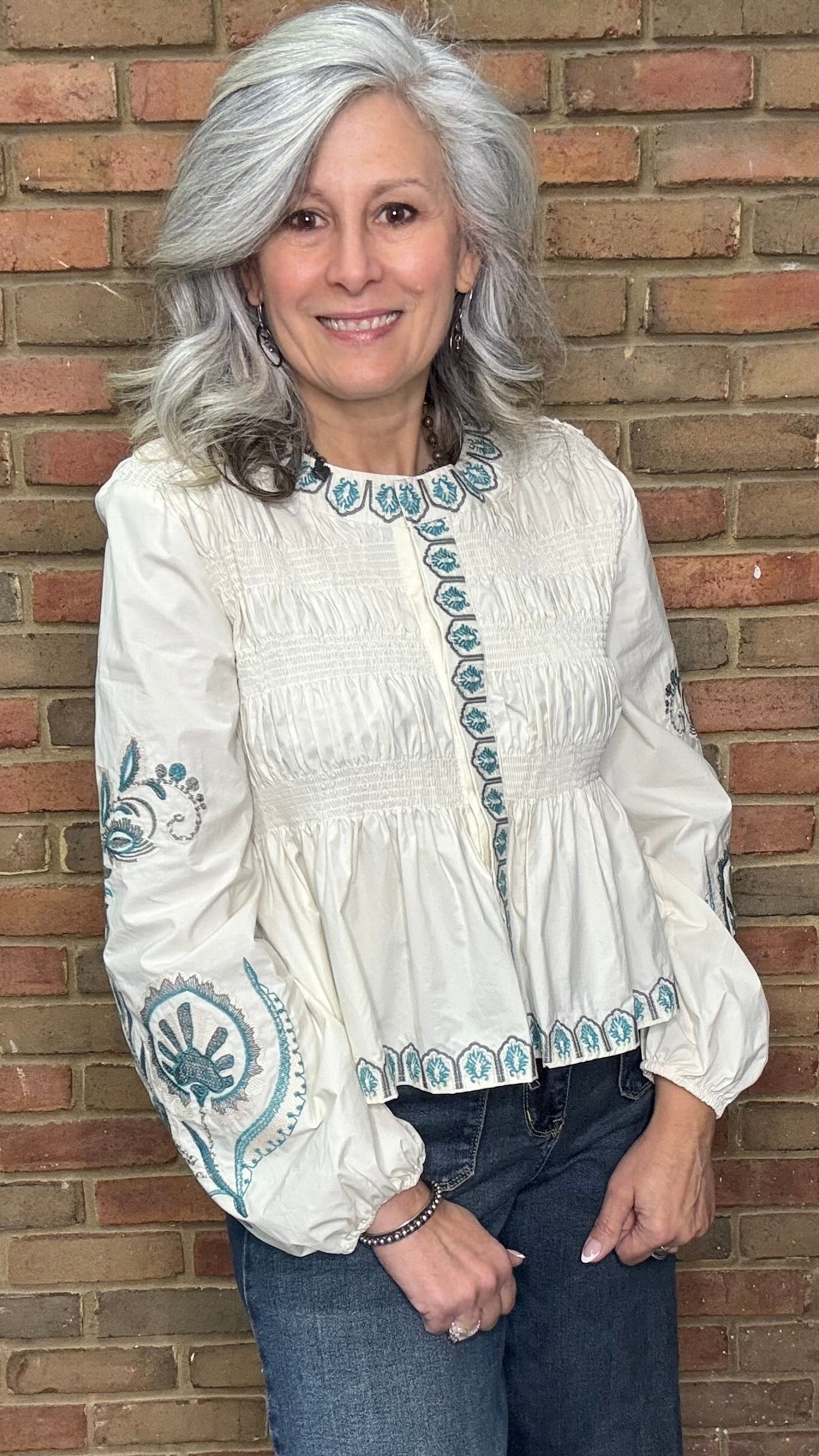Woman wearing the Embroideried Smocked Peasant Top and Judy Blue Palazzo jeans against a brick wall.