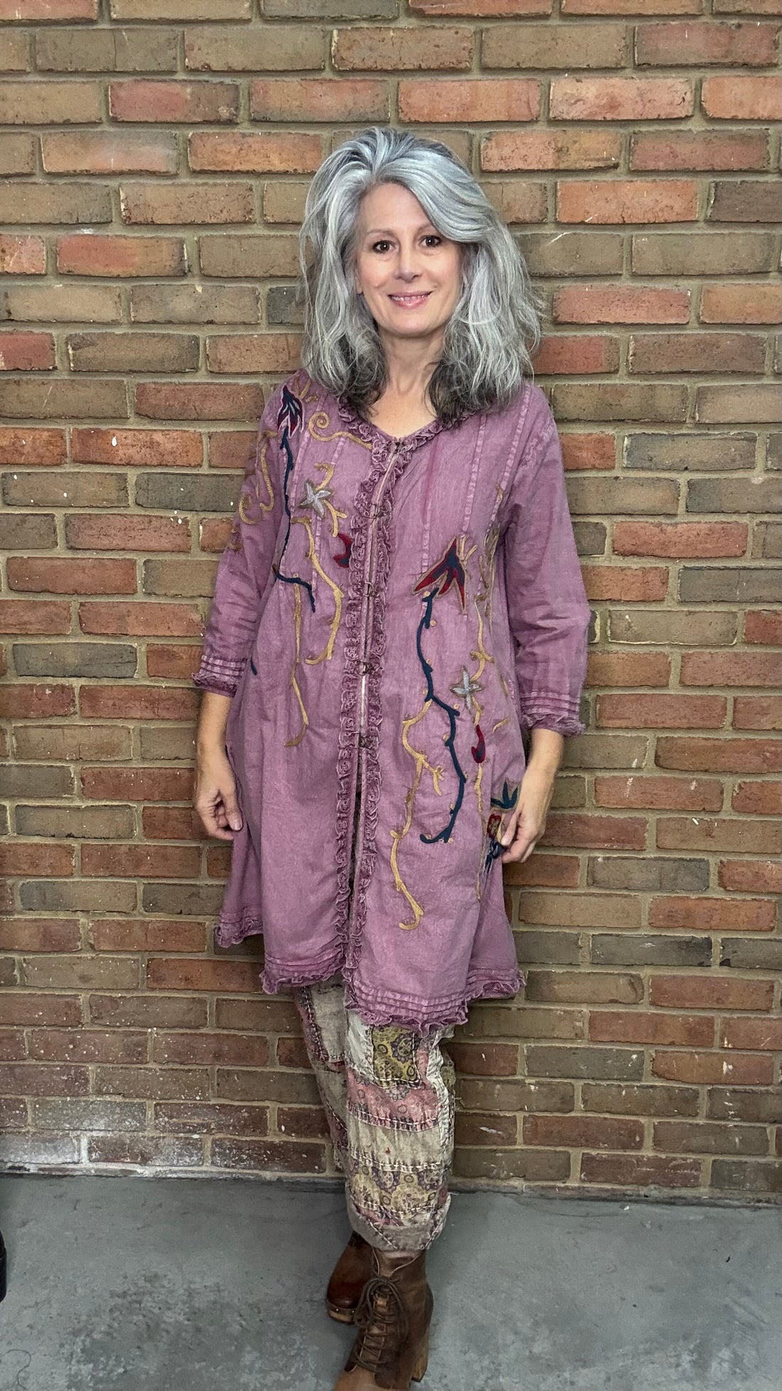 Woman in a purple embroidered dress standing against a brick wall