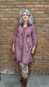 Woman in a purple embroidered dress standing against a brick wall