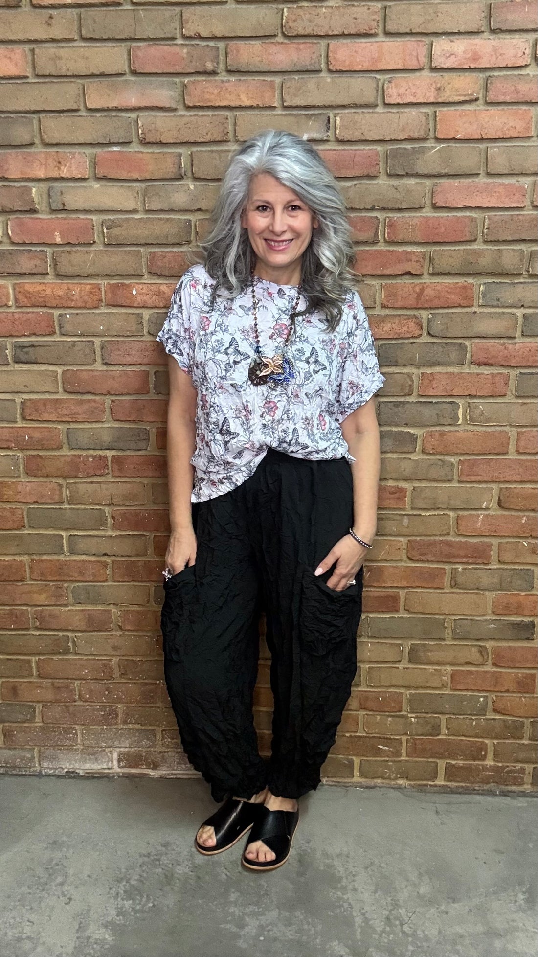 Person wearing Black Crinkle Side Pocket Pant and a patterned top against a brick wall.