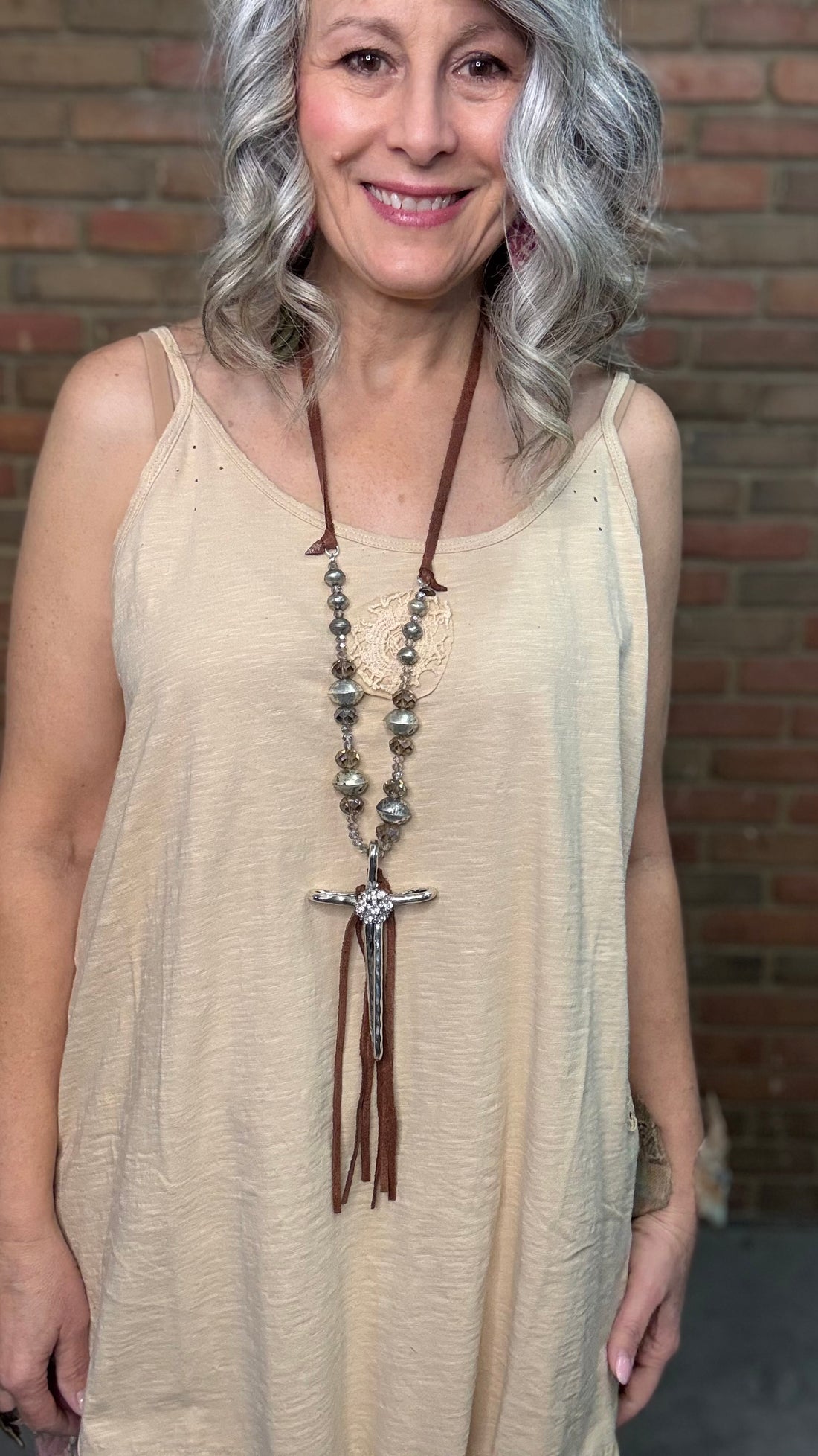 Woman wearing a beige sleeveless top with a Hammered Cross Necklace against a brick wall.