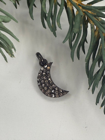 Crescent moon-shaped jewelry with gemstones on a light background with greenery