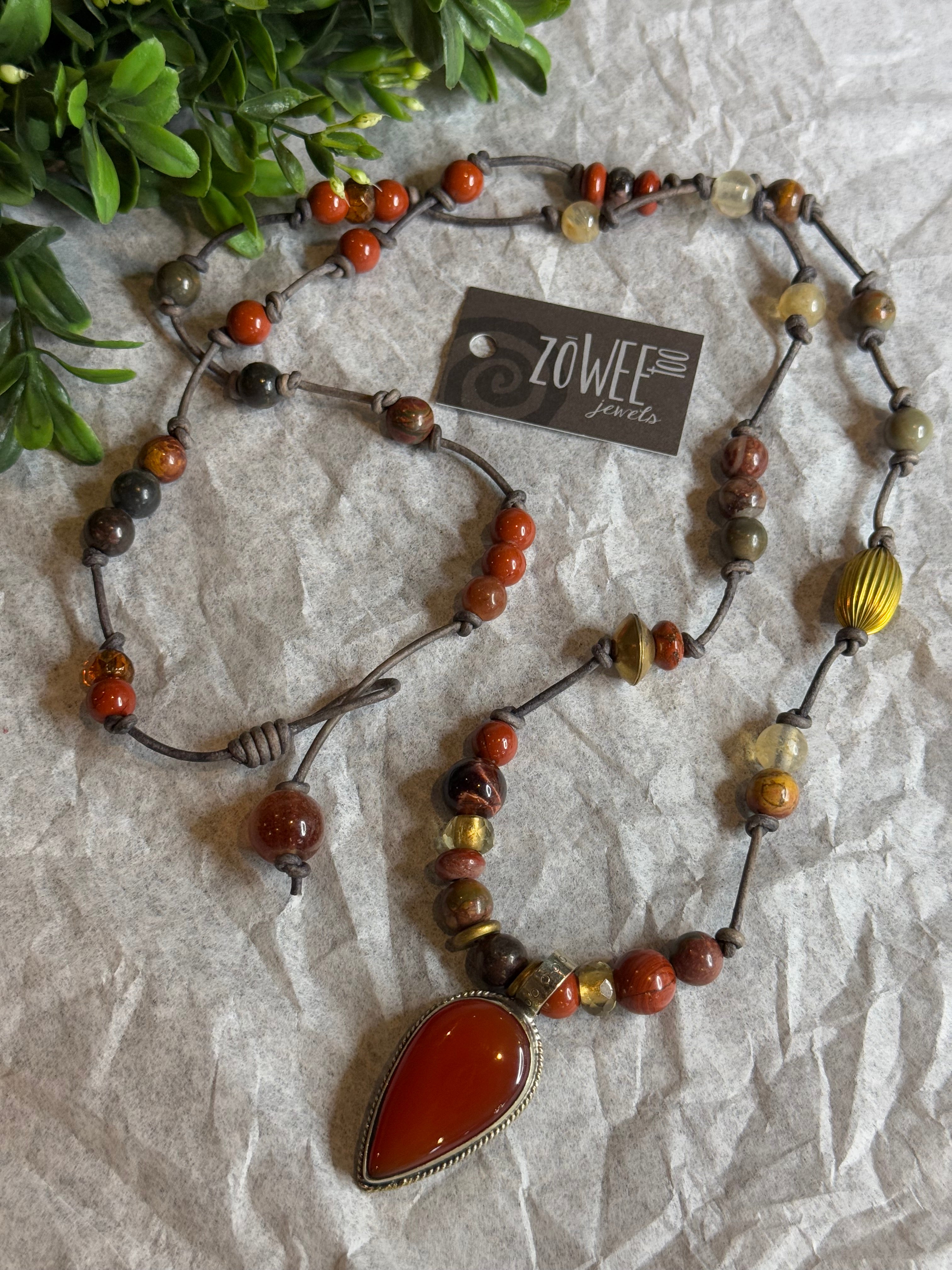 Beaded necklace with a large pendant on a textured surface, featuring a Zowee label.