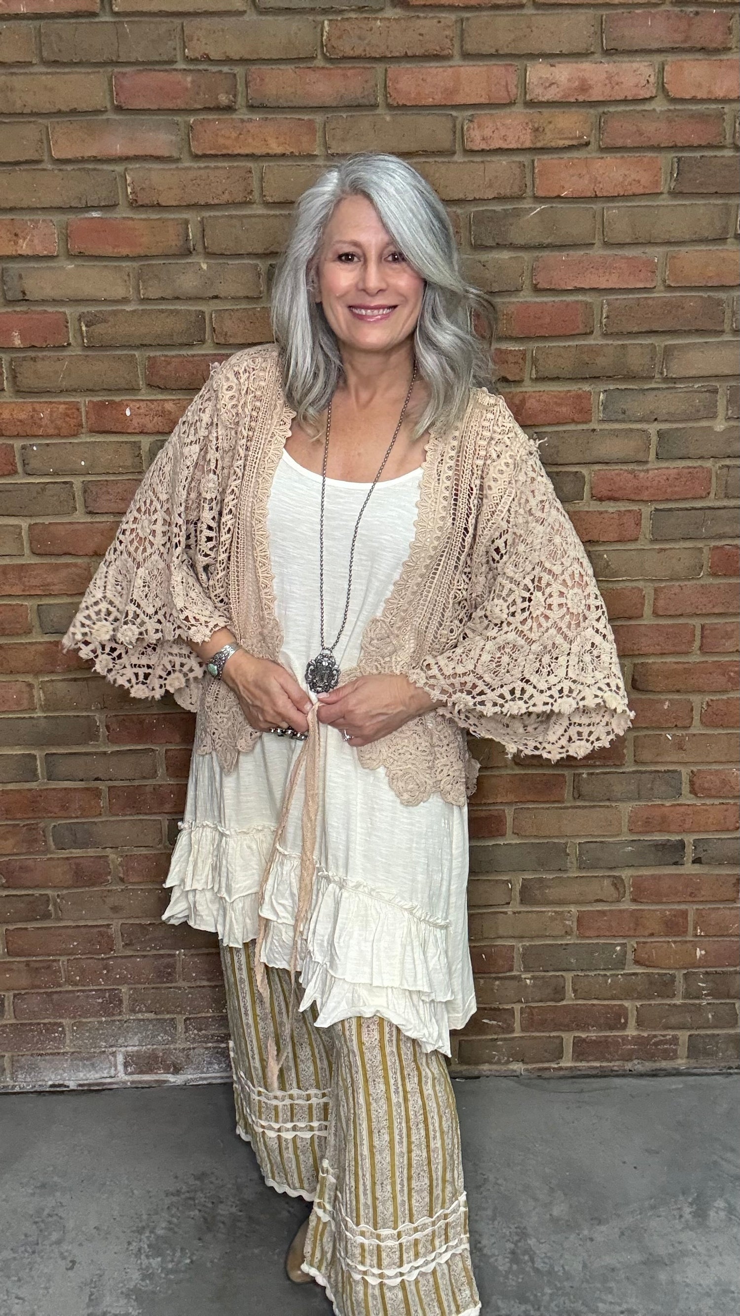 Woman wearing the crochet Forever Timeless Split Tails Jacket over a dress with striped pants standing against a brick wall.