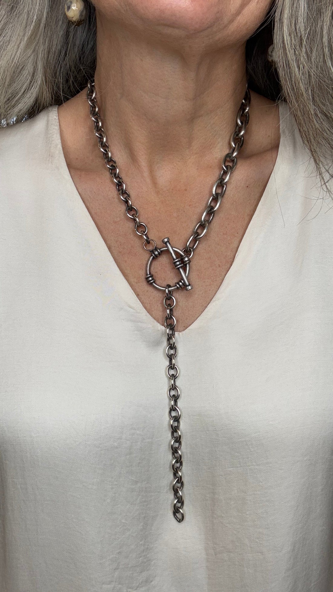 Close-up of a person wearing a delicate chain necklace with a white garment.
