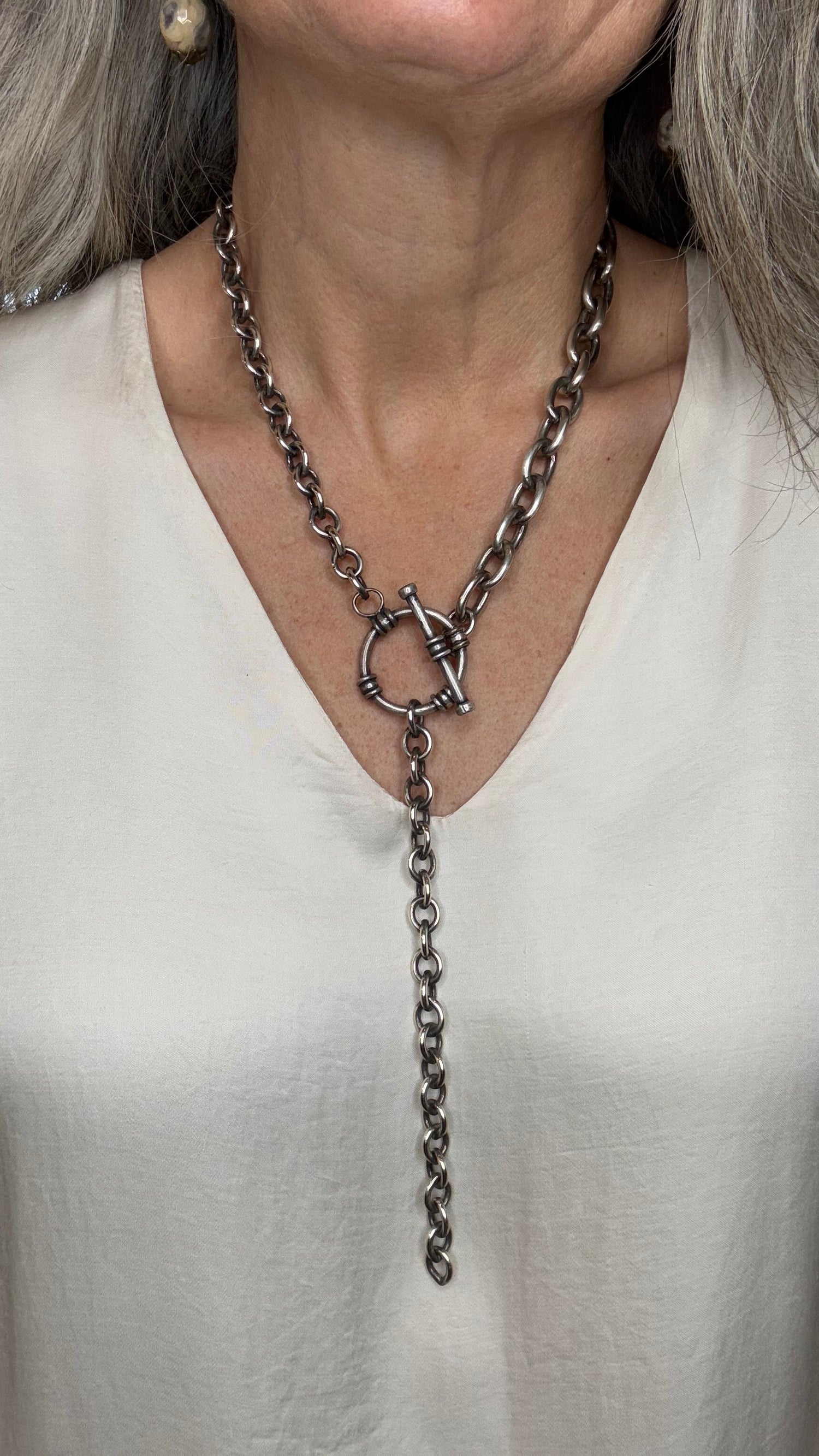 Close-up of a person wearing a delicate chain necklace with a white garment.