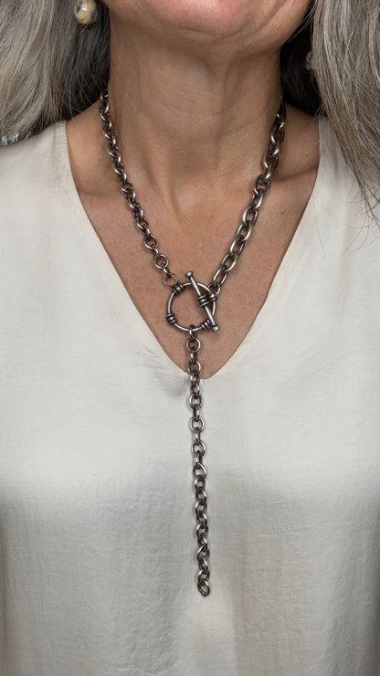 Close-up of a person wearing a delicate chain necklace with a white garment.