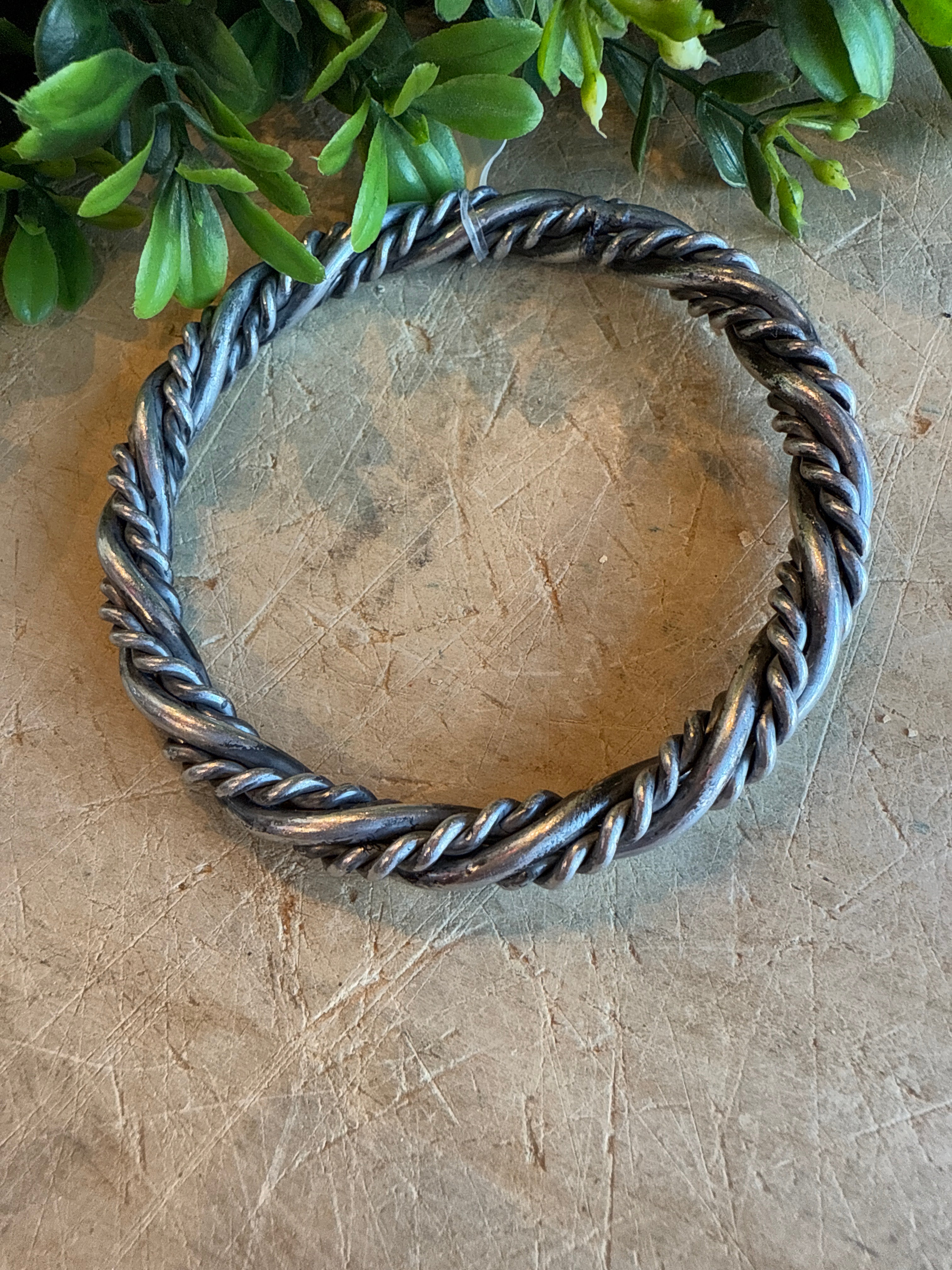 Silver Twist Bangle Bracelet on a textured surface with greenery.