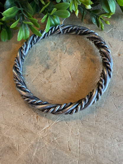 Silver Twist Bangle Bracelet on a textured surface with greenery.
