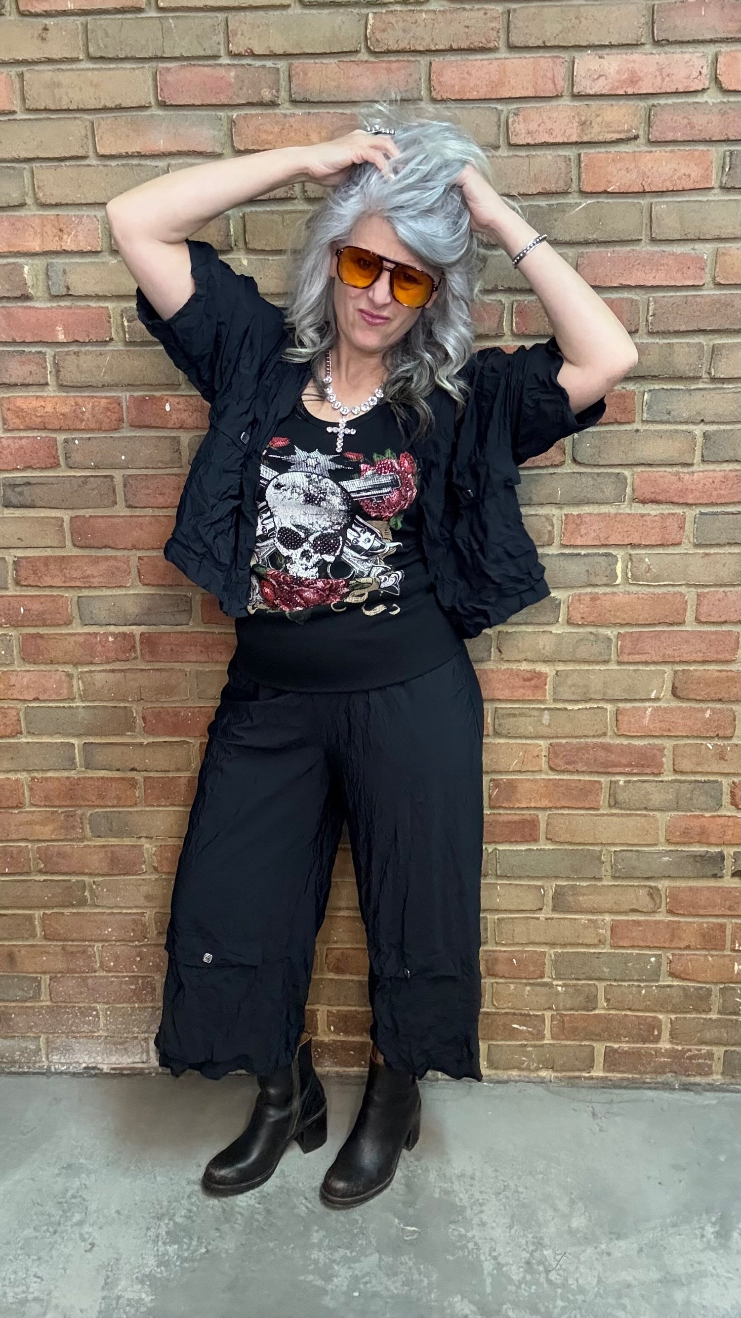 Woman standing against a brick wall wearing Francesca Jacket - Black, white top, and black pants.