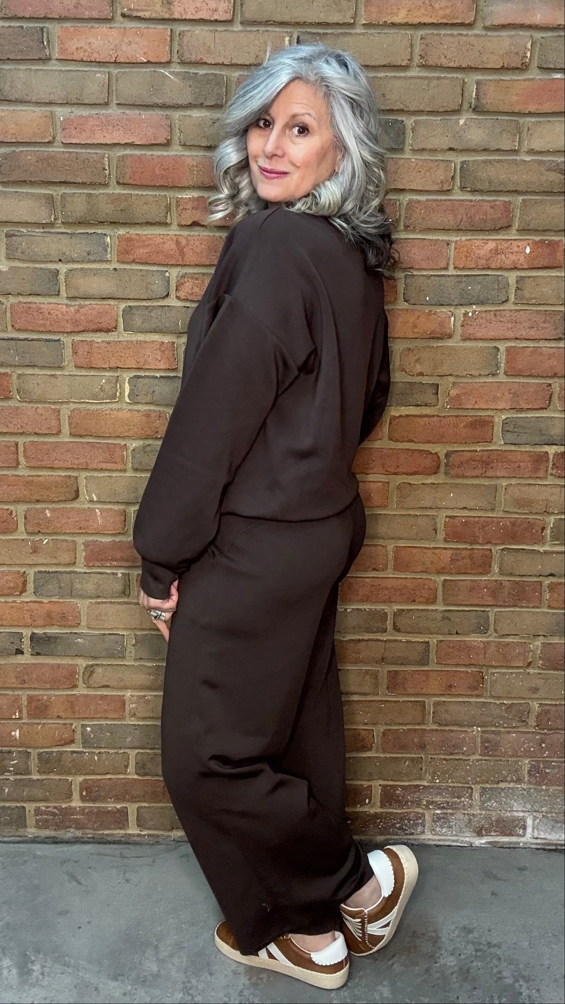 Person wearing a dark outfit leaning against a brick wall