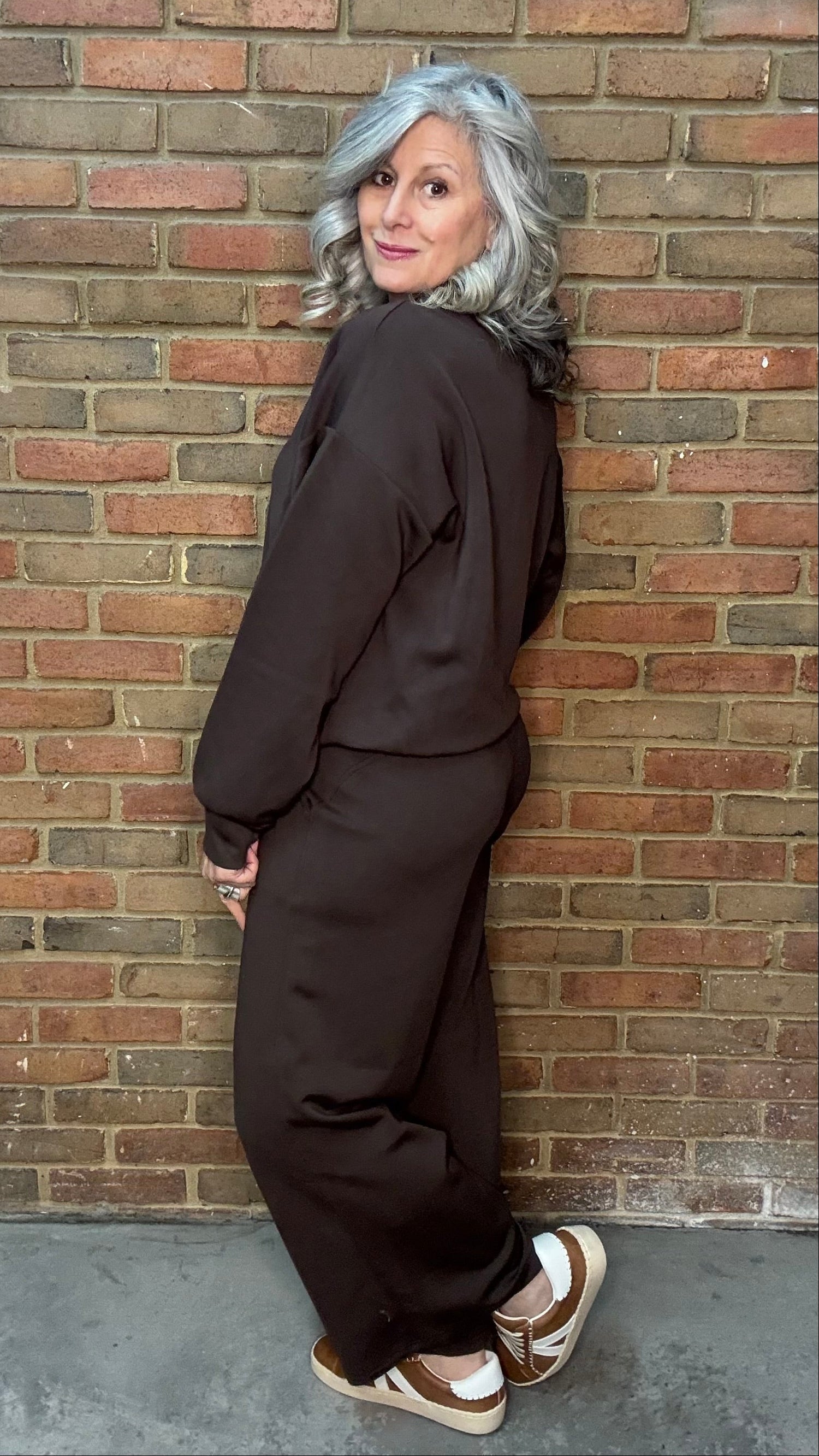 Person wearing a dark outfit leaning against a brick wall