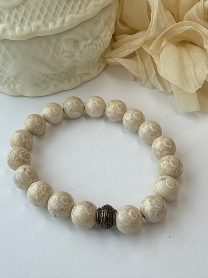 Beige beaded bracelet on a textured white surface with beige fabric and lace in the background