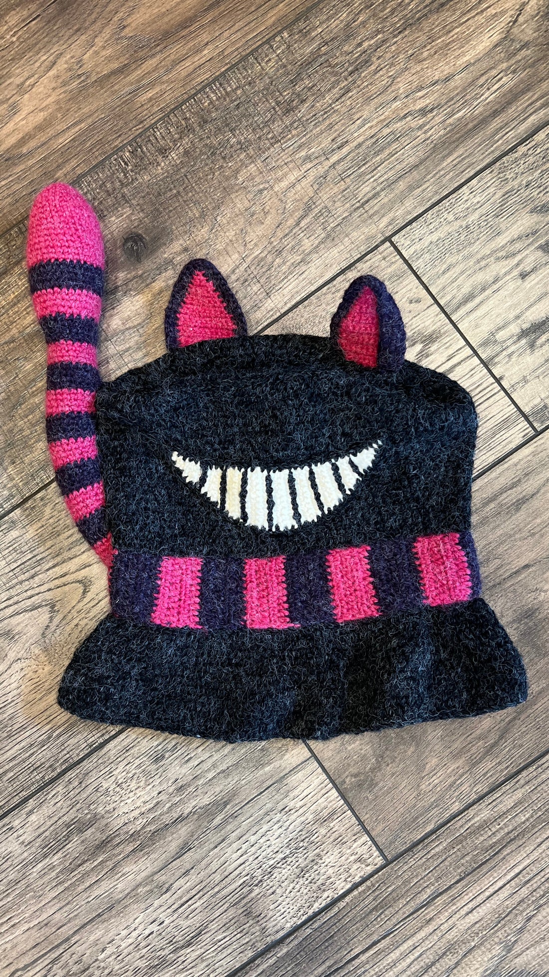 Knitted cat-shaped hat with pink and purple stripes on a wooden floor
