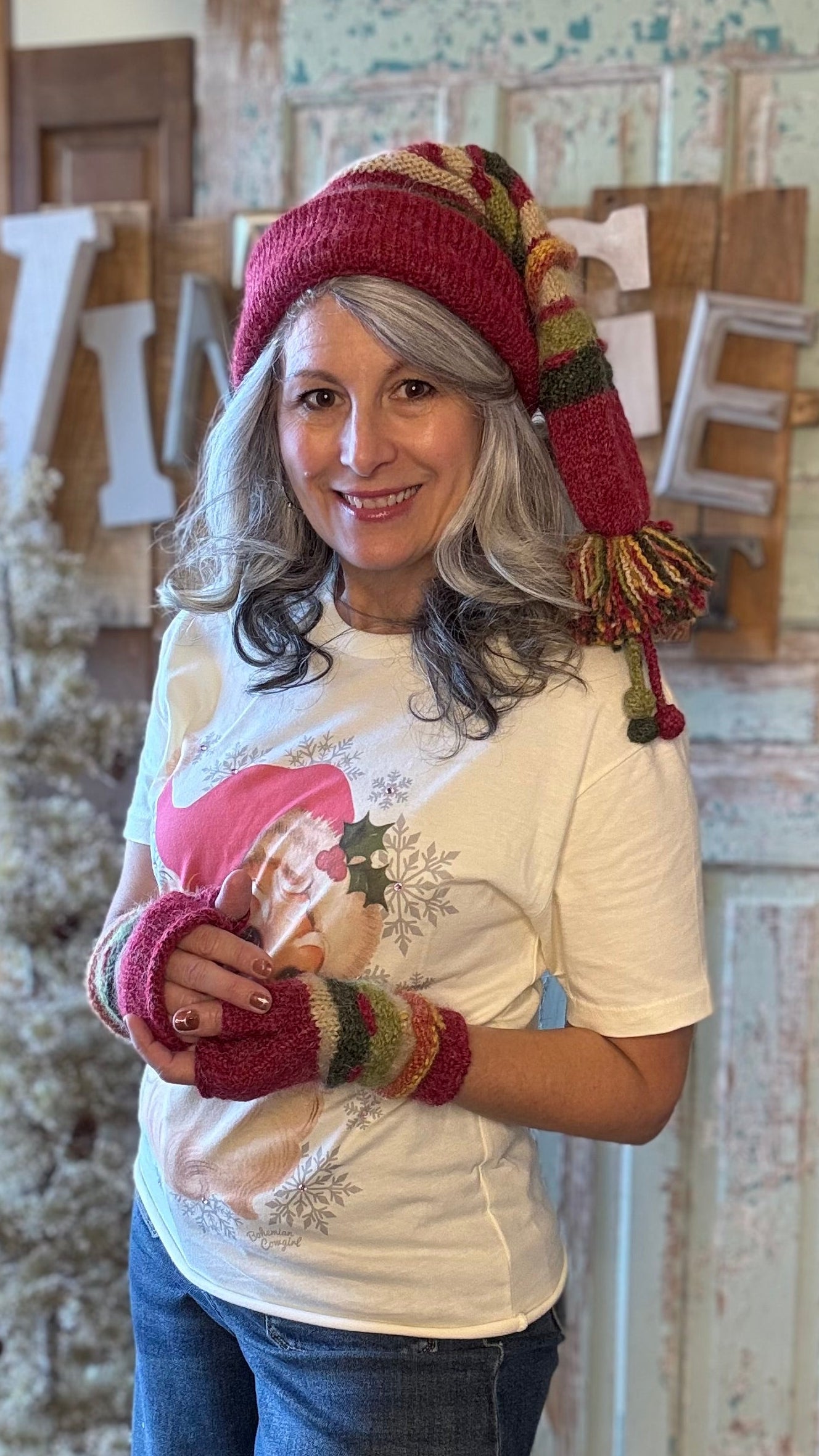 Woman wearing a colorful knitted hat and gloves indoors with decorative elements in the background.