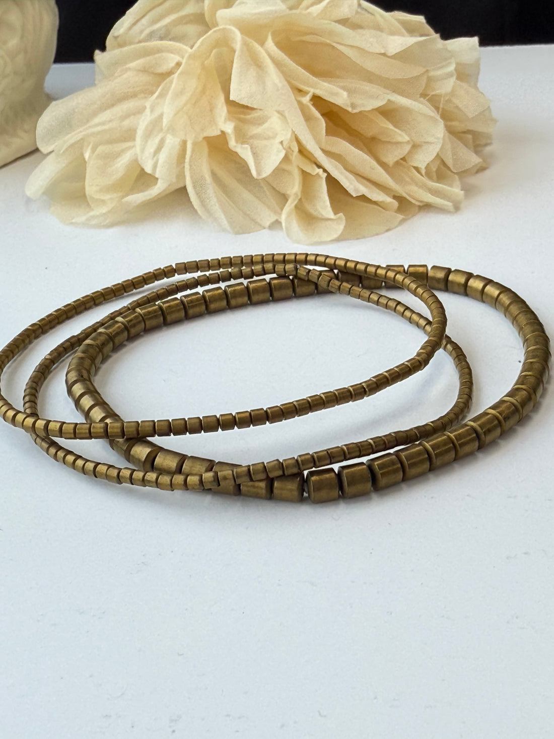 Bronze beaded bracelets and beige flower on a white background